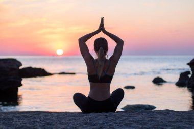 Kızın kumsalda büyük taşların arasında yoga eğitimi var. Denizde kayalar. gün doğumu