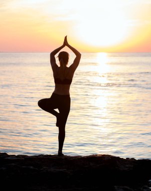 Kızın kumsalda büyük taşların arasında yoga eğitimi var. Denizde kayalar. gün doğumu