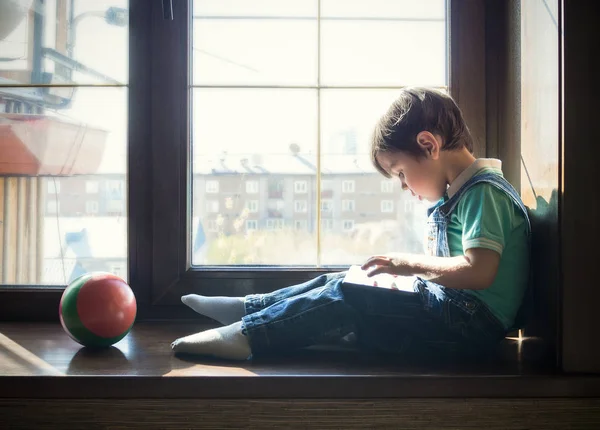 Çocuk pencere oturmak ve tablet kullanma — Stok fotoğraf