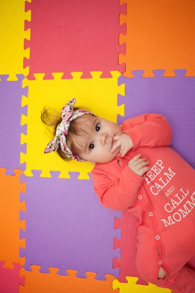 Adorable y elegante niña acostada en una alfombra de rompecabezas —  Fotos de Stock