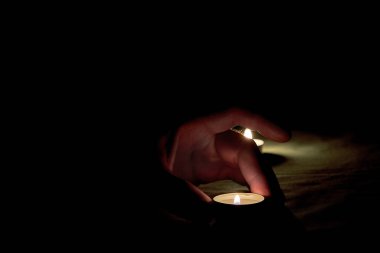 İnsan eli masanın üzerine yanan bir mum koyar. Karanlıkta yanan bir mumun yanına.