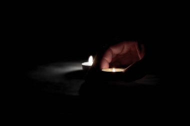 Yanan iki mum ve yanan bir mum tutan bir insan eli görülüyor.