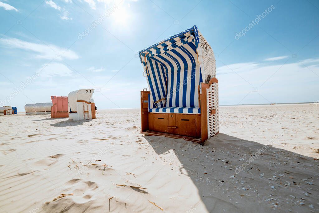 Blue and white striped roofed wicker beach chair in backlight. White sandy tropical beach in hot summer sunshine. Travelling and summer vacation concept