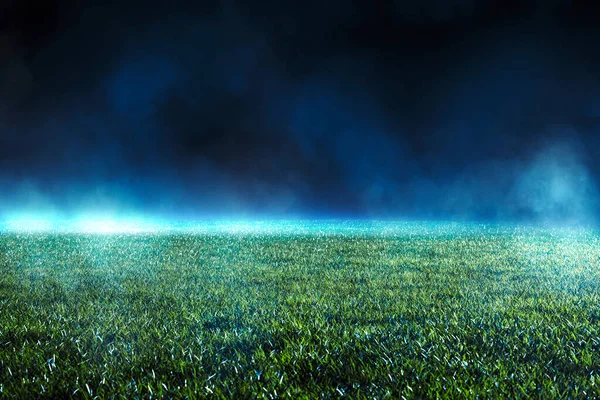 Night low view of maintained lawn at football stadium. Beams of light showing light effects at fog.