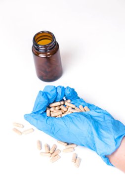 Doktor, cam bir kaptaki eldivenle eline tablet döküyor.