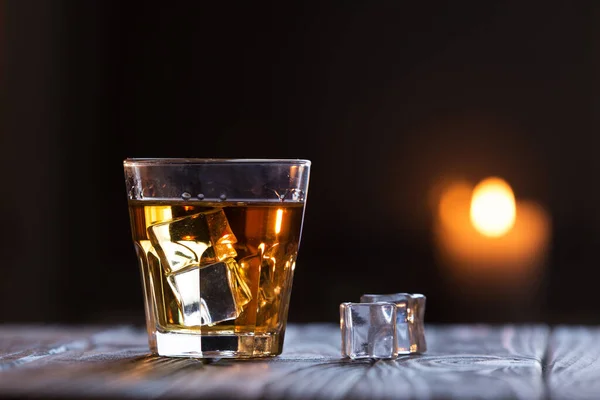 Glass of scotch whiskey and ice on dark background