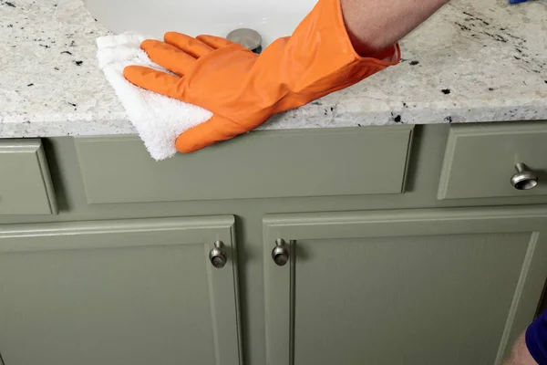 Mano usando un guante naranja limpiando un mostrador de baño de piedra —  Fotos de Stock