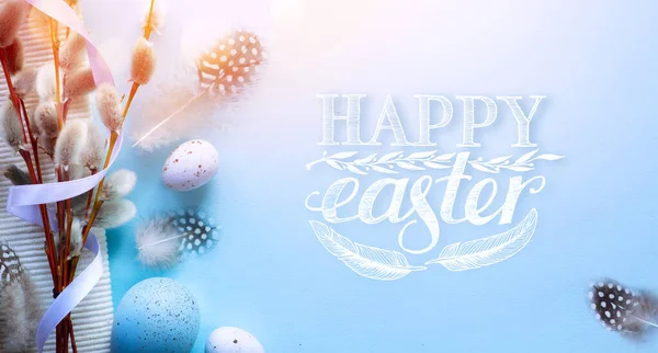 Art Happy Easter risen;  Easter eggs, Spring Flowers and bird feather on blue background; Holiday Easter banner or greeting card background