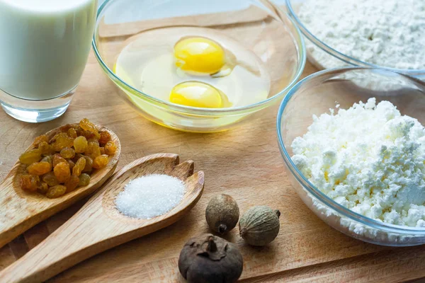 cheese, sugar, flour, eggs, wooden spoons, raisins, on a wooden background