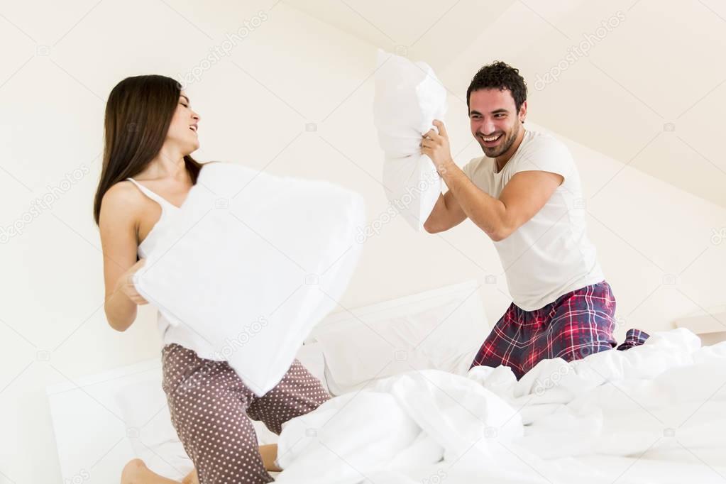 Mature couple kneeling on bed having pillow fight high