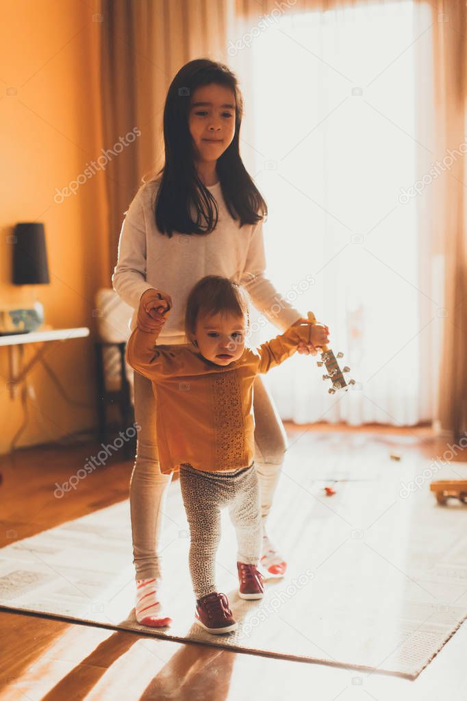 Girl helping baby sister to walk