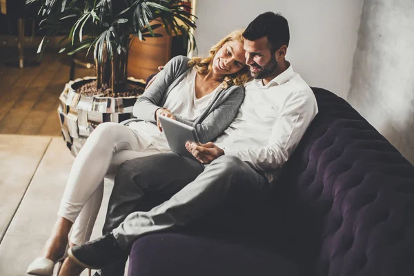 Casal sentado no sofá e olhar no tablet — Fotografia de Stock