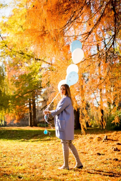 Вагітна жінка з повітряними кулями в осінньому лісі — стокове фото