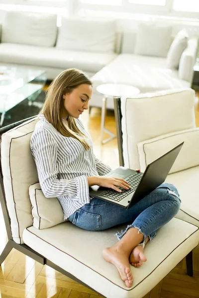 Mujer usando un ordenador portátil mientras se relaja en el sofá de la habitación — Foto de Stock