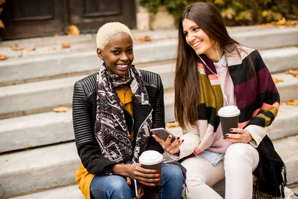 Young multiracial friends sitting in autumn park, talking and carry coffee to go in the hands
