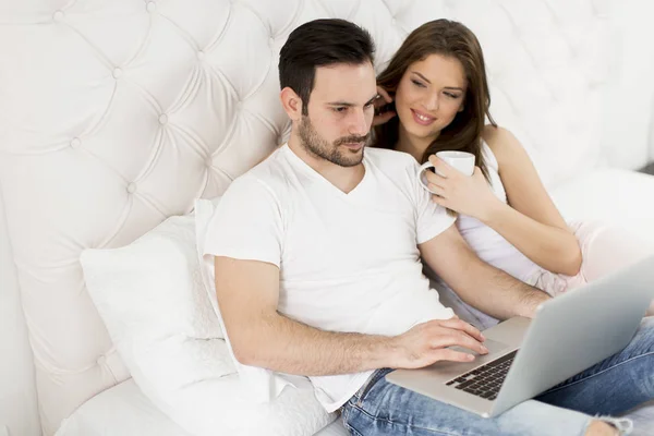 Alegre pareja usando un portátil acostado en su cama en casa —  Fotos de Stock