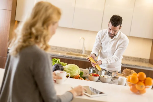 Muž připravuje jídlo, zatímco mladá žena sedí a využívání tabl — Stock fotografie