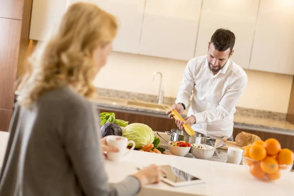 Hombre preparando una comida mientras una joven sentada y el uso de tabl — Foto de Stock