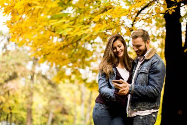 Bir akıllı telefon izliyor ve sonbahar parkta duran Çift