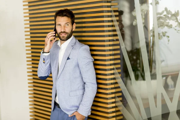 Красивый молодой бизнесмен пользуется телефоном в офисе — стоковое фото