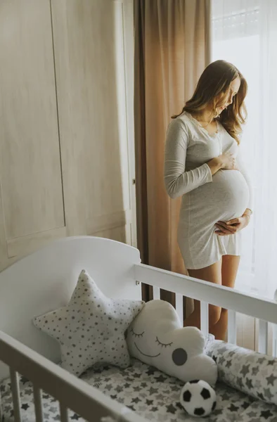 Молода вагітна жінка біля колиски — стокове фото