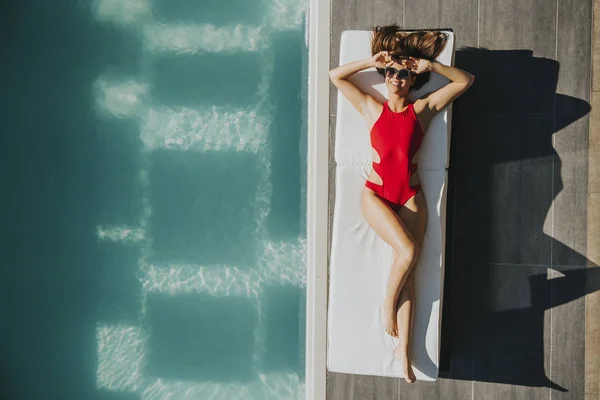 Mujer joven acostada junto a la piscina — Foto de Stock