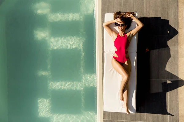 Молодая женщина лежит у бассейна на шезлонге — стоковое фото