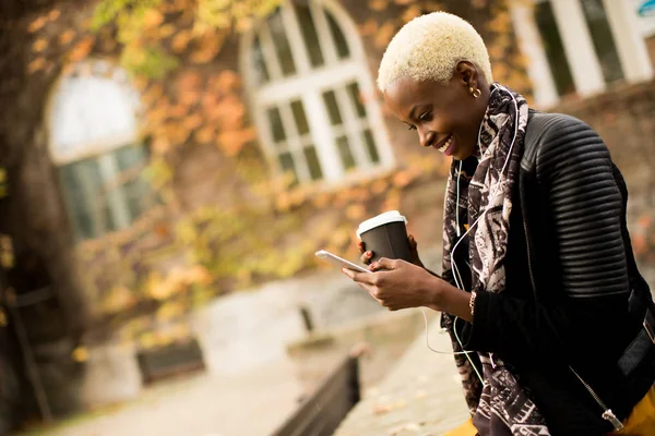 Kahve fincanı ve cep telefonu sokakta olan siyah kadın