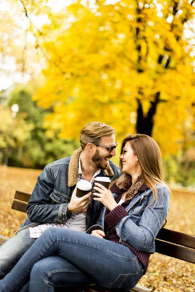 对年轻夫妇在秋天杯咖啡坐在板凳上坐 — 图库照片
