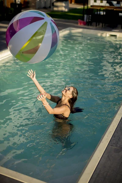 Jonge vrouw spelen met een bal in het zwembad — Stockfoto