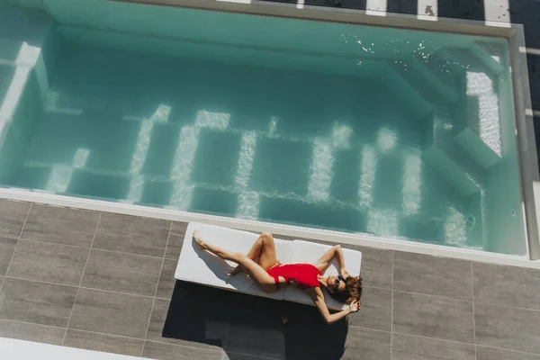 Mujer joven tumbada junto a la piscina en la tumbona — Foto de Stock