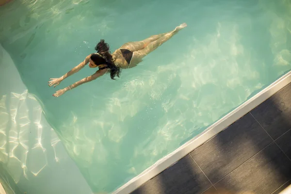 Vrouw in bikini drijvend op het water in het zwembad — Stockfoto