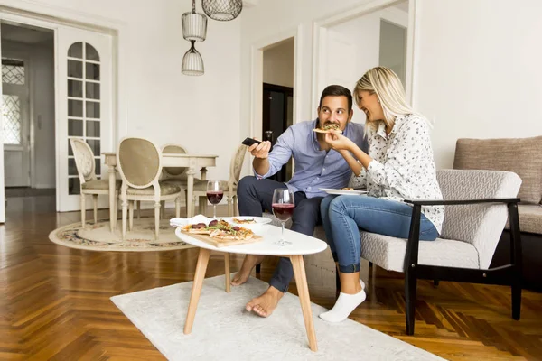 Jong koppel genieten van het eten van pizza en tv kijken — Stockfoto