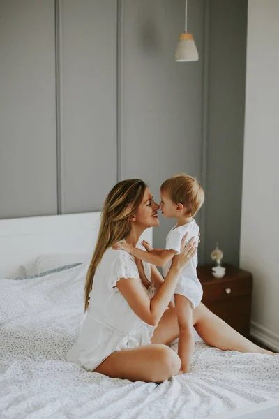 Ung glad mamma spelar i en vit säng — Stockfoto