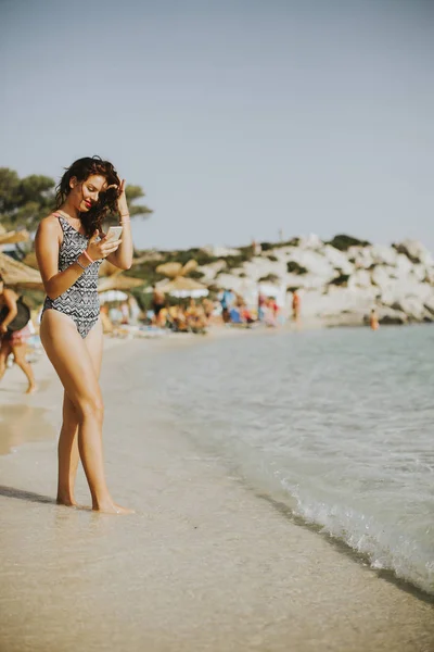 Jovem mulher atraente andando na praia e usando um p móvel — Fotografia de Stock