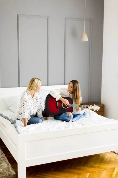 Дві молоді жінки з гітарою на ліжку — стокове фото