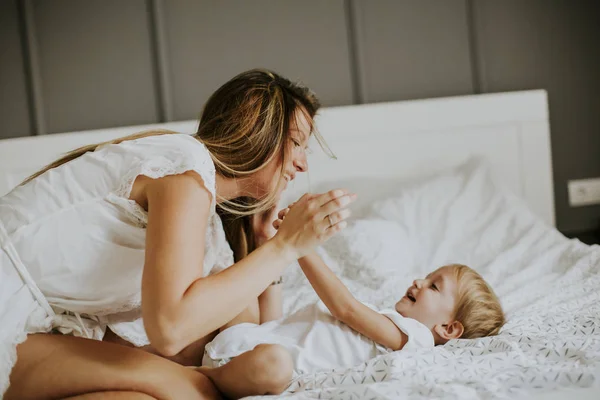 Jovem mãe feliz brincando em uma cama branca — Fotografia de Stock