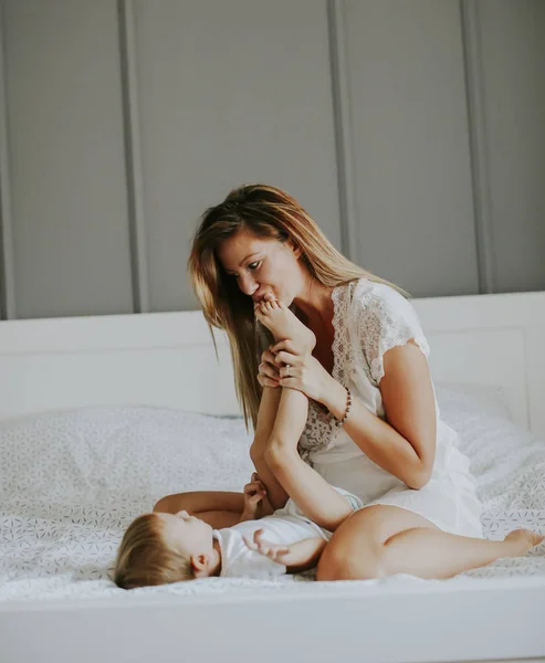 Junge glückliche Mutter spielt in einem weißen Bett — Stockfoto