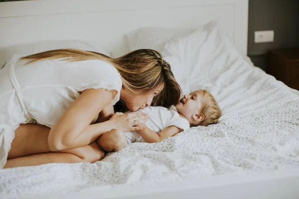 Jovem mãe feliz brincando em uma cama branca — Fotografia de Stock