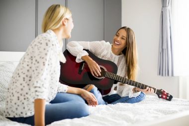 İki genç kadın yatakta gitar ile