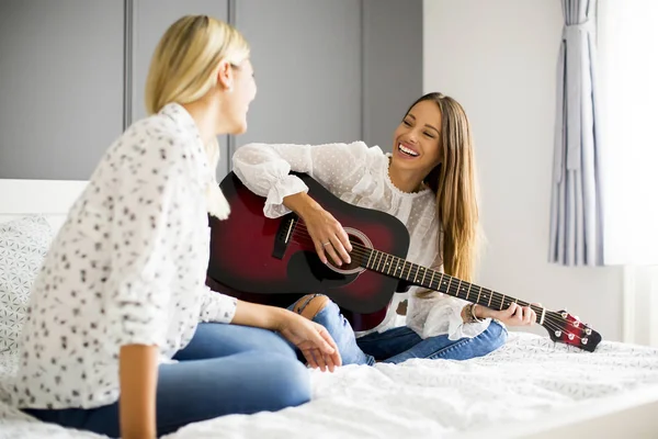 İki genç kadın yatakta gitar ile