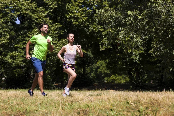 Güneşli bir günde parkta koşan genç bir çift.