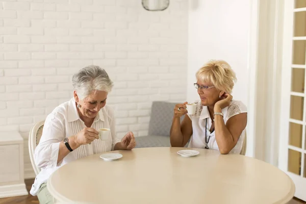 Two older women drinking coffe at home and talking