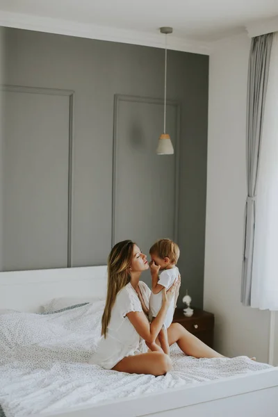 Junge glückliche Mutter spielt in einem weißen Bett — Stockfoto