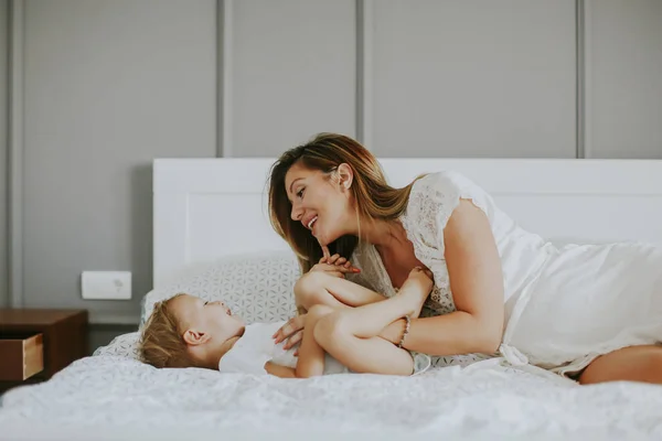 Mãe brincando com o menino na cama no quarto — Fotografia de Stock