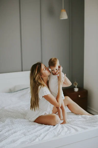 Jovem mãe feliz brincando em uma cama branca — Fotografia de Stock