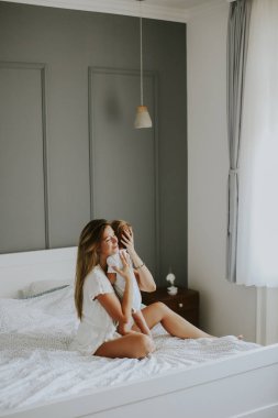 Beyaz yatakta oynayan genç mutlu anne