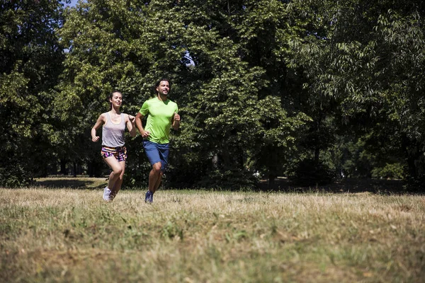 Güneşli bir günde parkta koşan genç bir çift.
