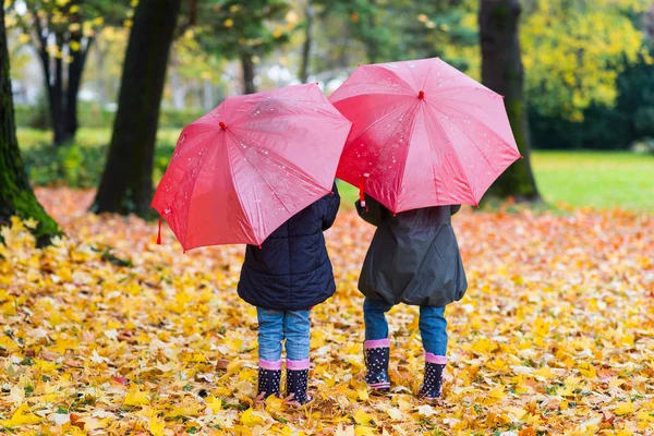 Kleine Mädchen laufen mit roten Regenschirmen — Stockfoto