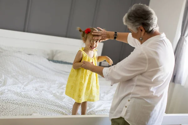Mormor leker med ett litet barnbarn på sängen — Stockfoto